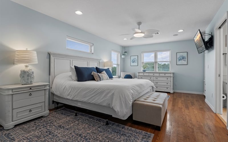 Spacious master ensuite bedroom featuring a smart TV, cozy king-size bed, walk-in closet, chair, dresser, chest, and armoire, with all linens, including pool towels, provided.